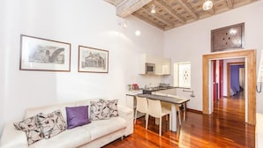 A living room with a sofa, a dining table, and chairs. There is a kitchen area with a microwave and a sink. - Frattina Exclusive Apartment (Rome)