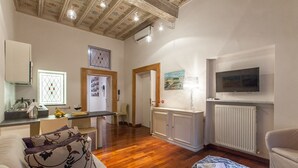 A spacious living area with wooden flooring, a kitchen with a sink and counter, a dining table with chairs, a sofa, and a television mounted on the wall. - Frattina Exclusive Apartment (Rome)