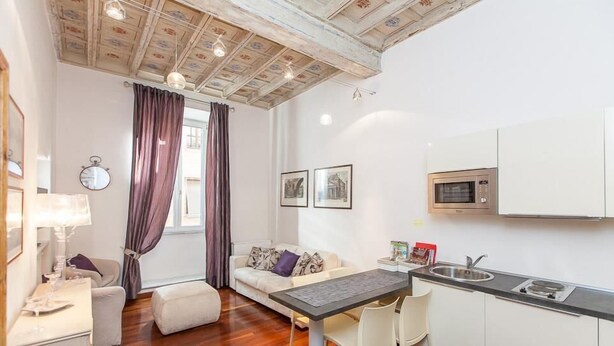 A compact living space with a kitchenette, a sofa, a dining table, and a window with curtains. - Frattina Exclusive Apartment (Rome)