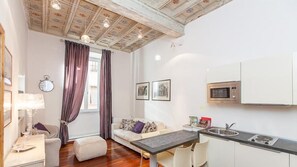 A compact living space with a kitchenette, a sofa, a dining table, and a window with curtains. - Frattina Exclusive Apartment (Rome)