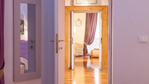 A hallway with a wooden door leading to a living area with a couch and a clock on the wall. - Frattina Exclusive Apartment (Rome)
