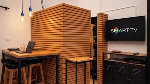 A modern kitchen with a wooden partition, a laptop on the counter, bar stools, a TV, and a cabinet with a Guinness logo. - Nilo's Flat - Location in the historic center of Naples  (Napoli)