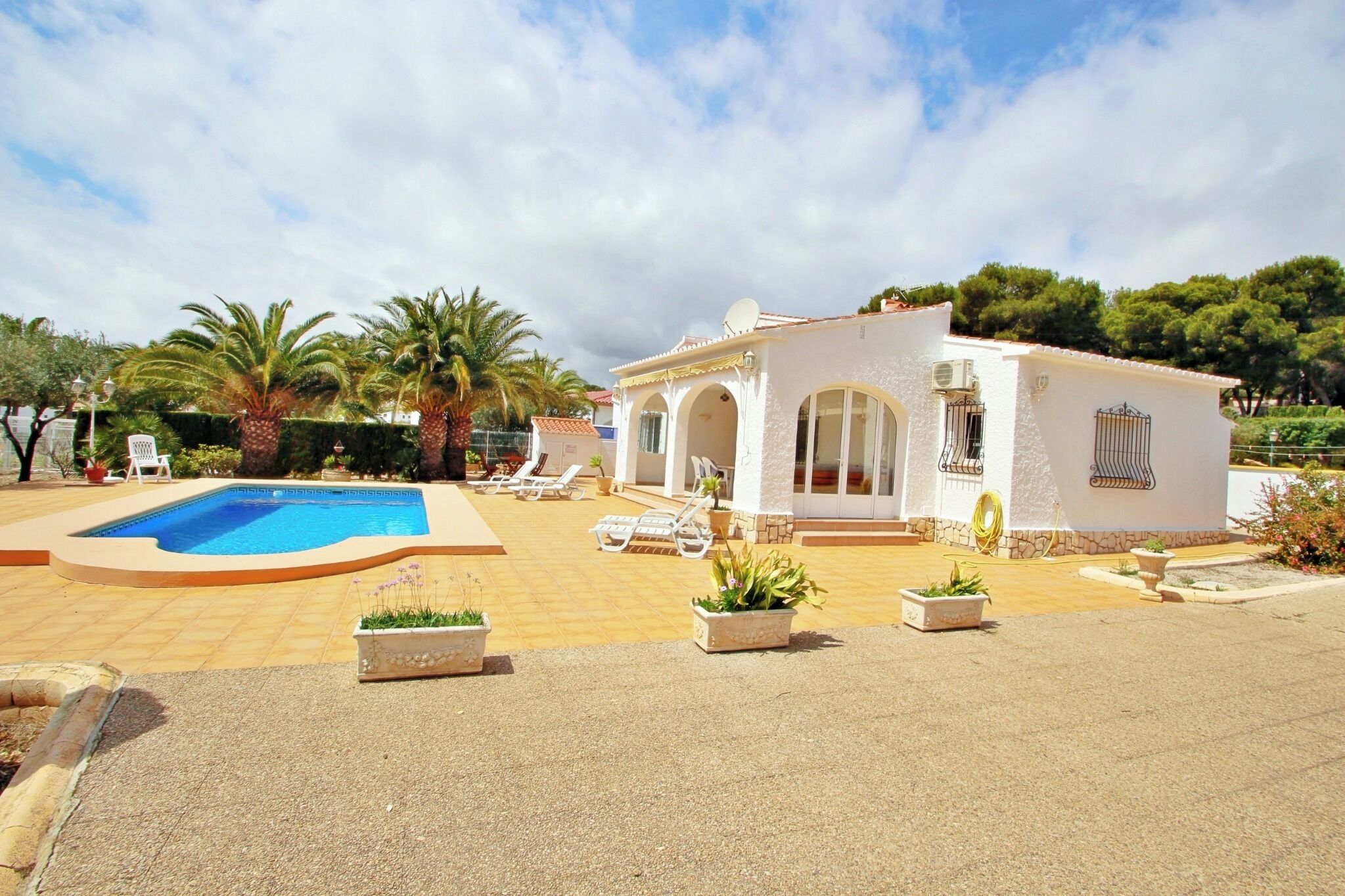 A villa with a swimming pool, sun loungers, and a garden with palm trees.