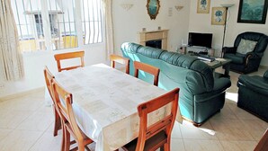 A living room with a green sofa, a dining table with chairs, a fireplace, and a television. - Albertina - pool & garden, close to beach (Benissa)
