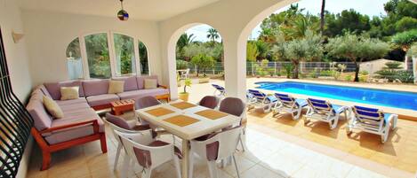 A sunlit outdoor living area with a pool, a sofa, a dining table, and lounge chairs.