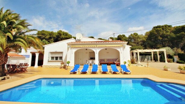 A pool area with blue lounge chairs, a covered seating area, and a white building with a tiled roof. - Albertina - pool & garden, close to beach (Benissa)