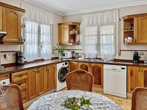 Une cuisine avec des meubles de rangement en bois, un lave-linge, un lave-vaisselle et une table à manger avec des chaises.