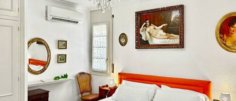Een hotelkamer met een bed, een kroonluchter, een schilderij, een spiegel en een raam.