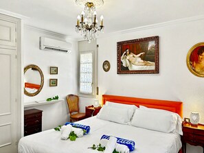 Une chambre d’hôtel avec un lit, un lustre, un tableau, un miroir et une fenêtre.