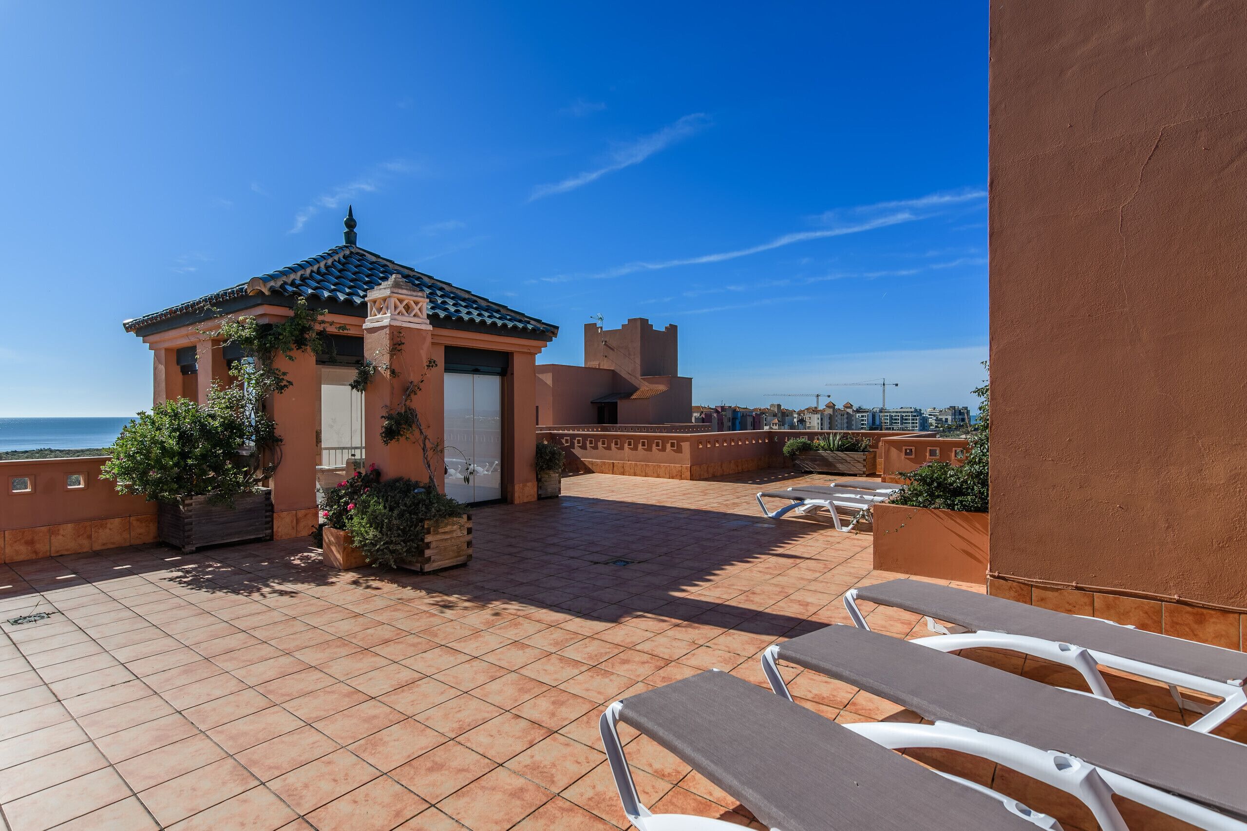 A rooftop terrace with tiled flooring, a small building with a tiled roof, and a view of the ocean.