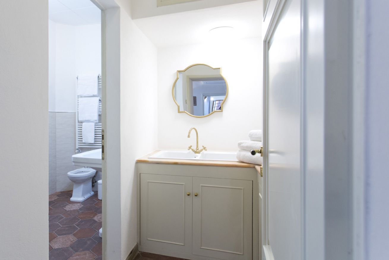 A bathroom with a white sink, gold faucet, and a round mirror with a gold frame.