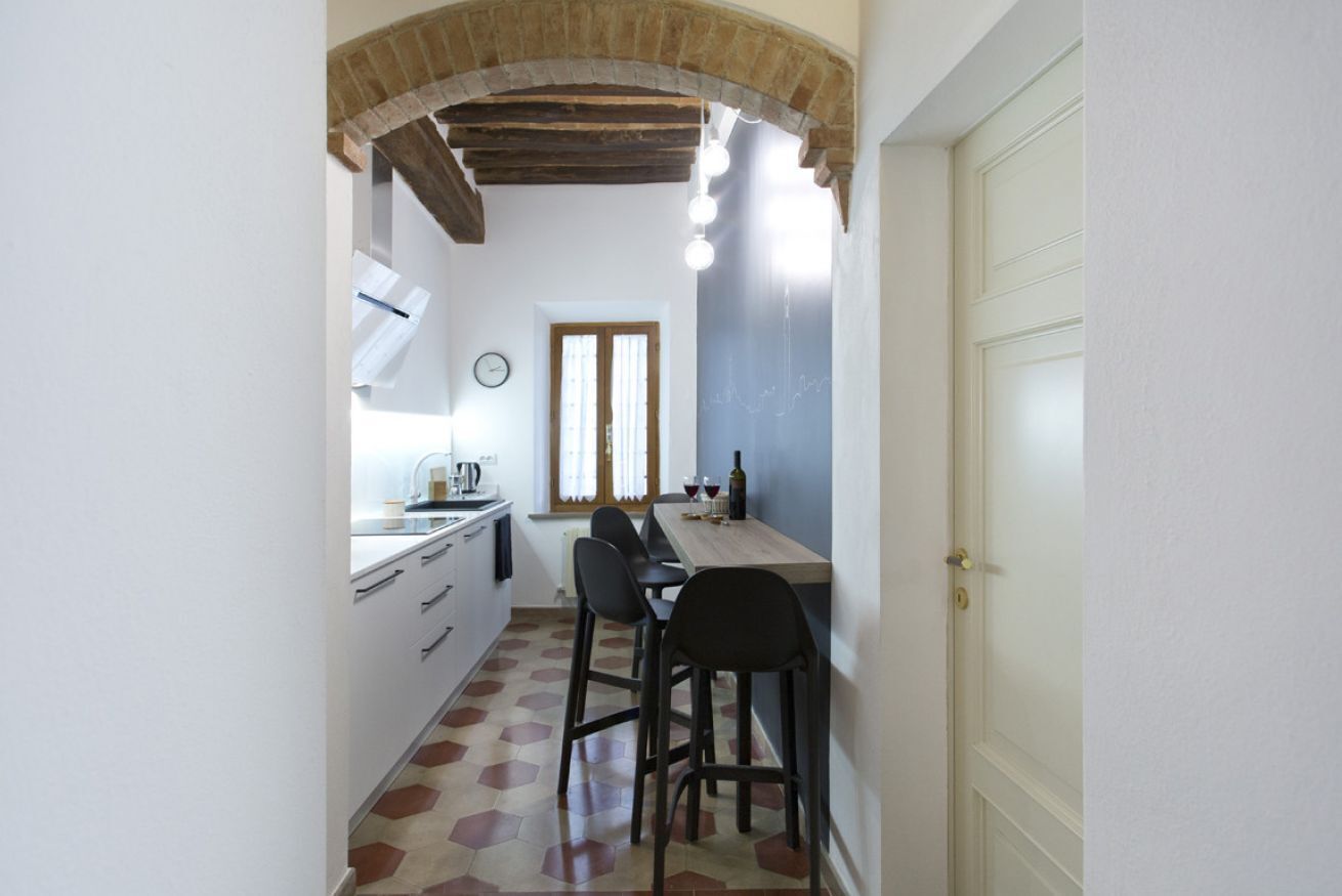 Una cocina estrecha con comedor, que destaca por su techo de madera, una ventana con cortinas y una puerta blanca.