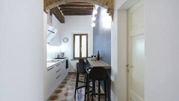 Una cocina estrecha con comedor, que destaca por su techo de madera, una ventana con cortinas y una puerta blanca.