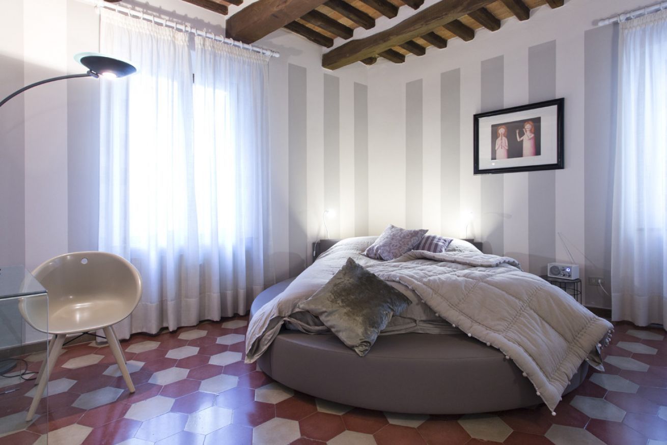 Un dormitorio con una cama redonda, una silla y un cuadro en la pared.