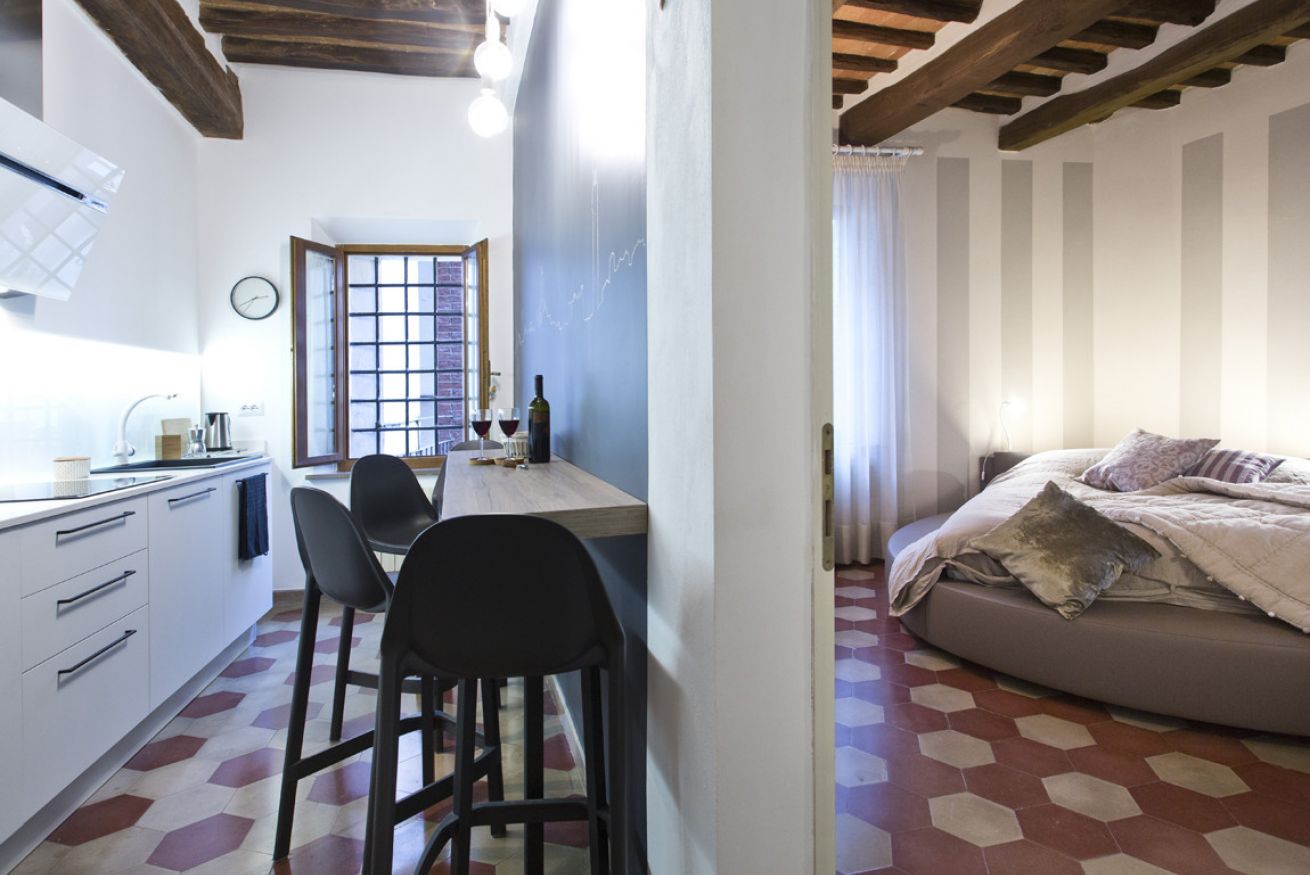 Una cocina compacta con zona de comedor, una cama con ropa de cama a rayas y un suelo con estampado hexagonal.