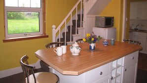 Una cocina con una isla de madera, armarios blancos, un microondas y una ventana con vistas a un campo verde.