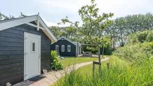 A wooden cabin with a door, a small deck with chairs, and a grassy yard. - This chalet is equipped with a gas fireplace and infrared sauna. (BURGH-HAAMSTEDE)