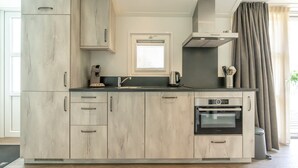 A modern kitchen with light wood cabinetry, a built-in oven, and a window with blinds. - This chalet is equipped with a gas fireplace and infrared sauna. (BURGH-HAAMSTEDE)