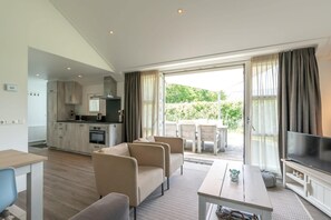 A modern living room with a sofa, a TV, and a dining area with a table and chairs. - This chalet is equipped with a gas fireplace and infrared sauna. (BURGH-HAAMSTEDE)