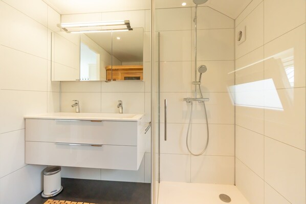 A modern bathroom with a glass-enclosed shower, a white vanity with two sinks, and a mirror above the vanity. - This chalet is equipped with a gas fireplace and infrared sauna. (BURGH-HAAMSTEDE)