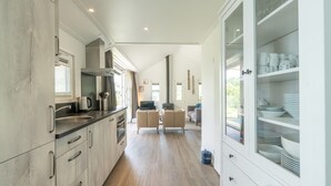 A modern kitchen with a wood floor, built-in cabinets, and a dining area with a sofa and chairs. - This chalet is equipped with a gas fireplace and infrared sauna. (BURGH-HAAMSTEDE)