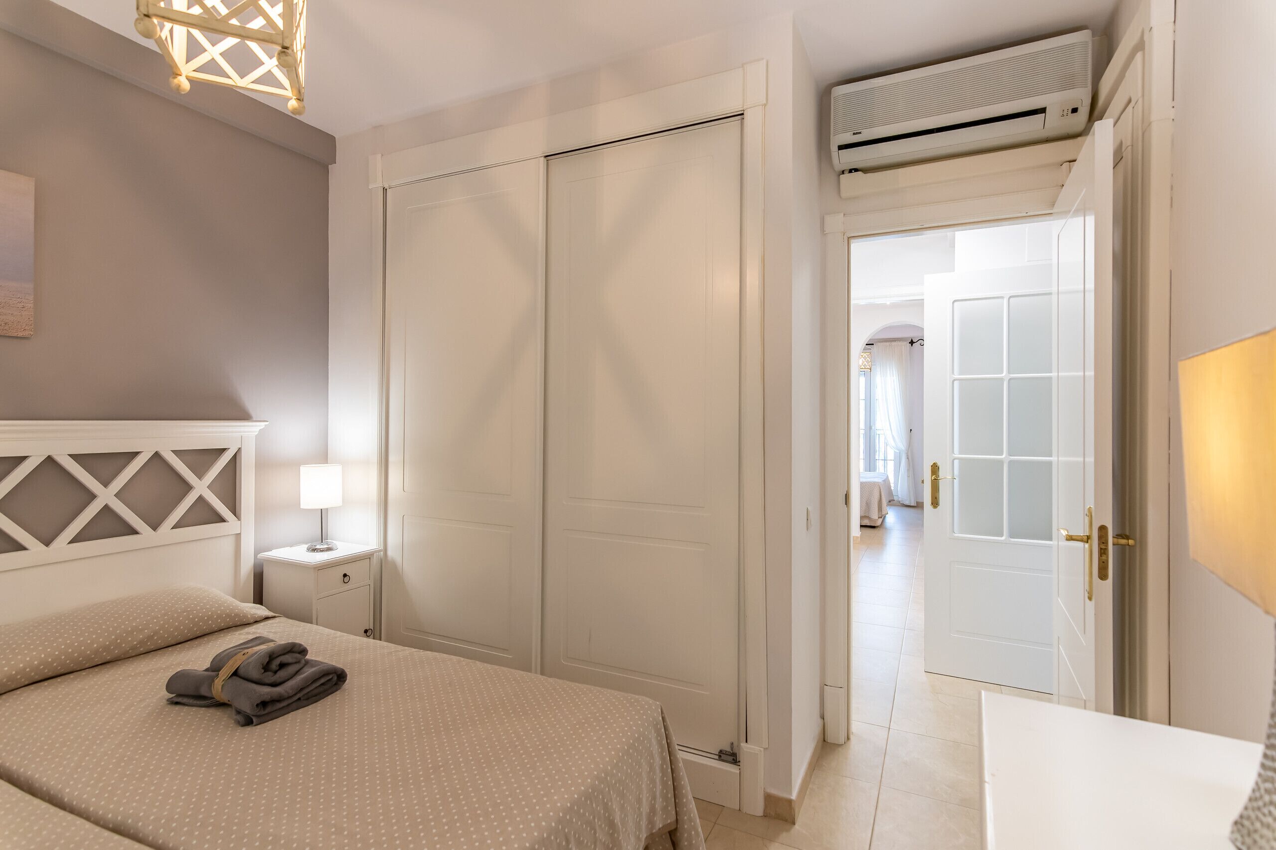 Een hotelkamer met een bed, nachtkastje, lamp en garderobe.