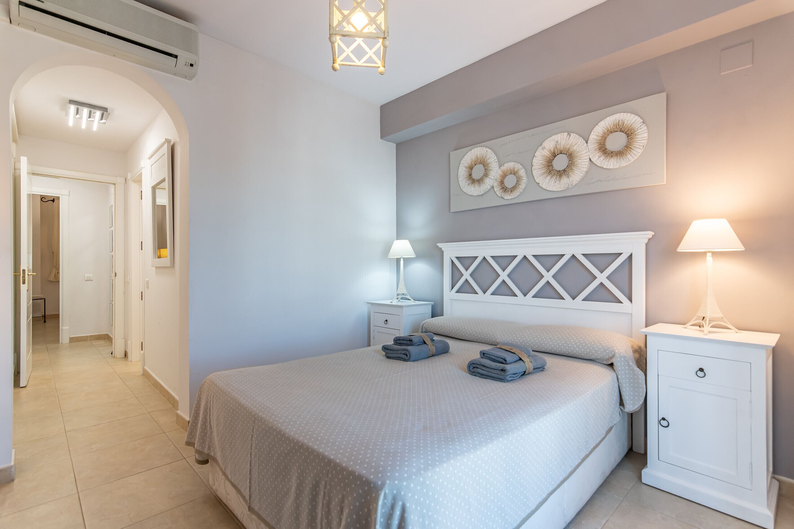 Un dormitorio con una cama, dos mesitas de noche, una lámpara de pared y un ventilador de techo.