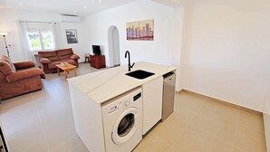 Un espace de vie compact comprenant un coin cuisine, un lave-linge, un canapé et une table à manger.