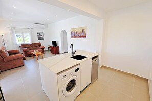 A compact living space with a kitchenette, a washing machine, a sofa, and a dining table.