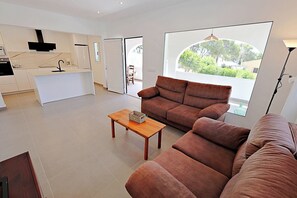 A modern living room with a brown sofa, a wooden coffee table, and a large window with a view of greenery.