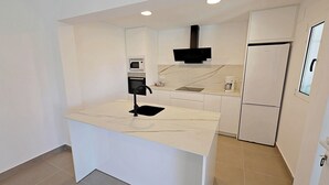 Une cuisine moderne dotée d’un plan de travail en marbre, d’un four encastré, d’un four à micro-ondes et d’un réfrigérateur.