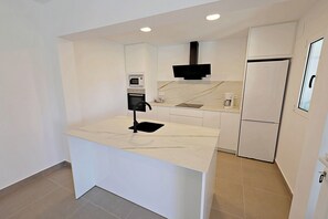 A modern kitchen with a marble countertop, built-in oven, microwave, and a refrigerator.