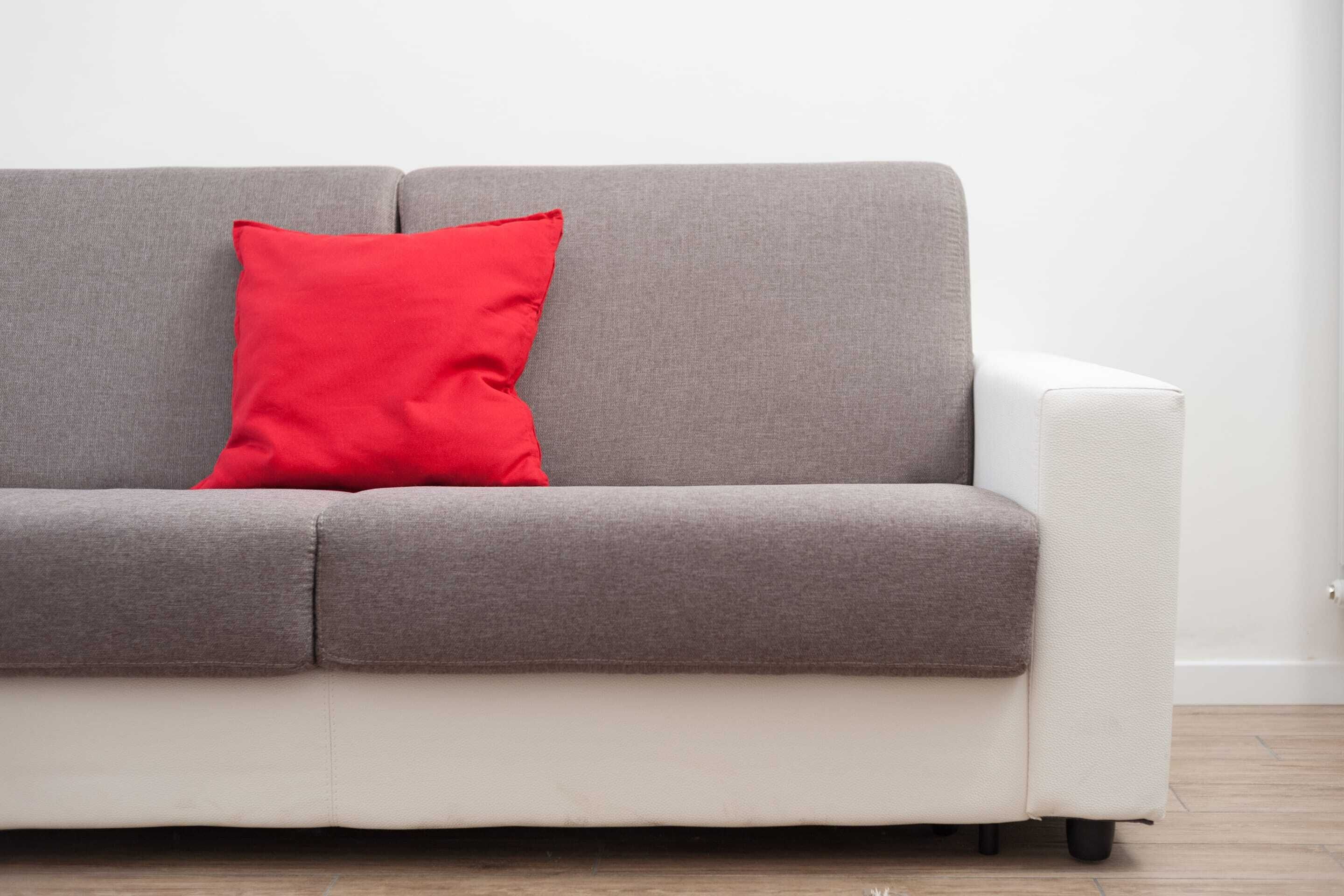 Un canapé gris et blanc avec un coussin rouge.