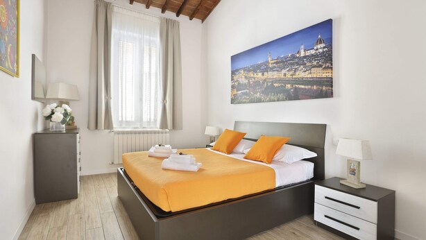 Una camera da letto moderna con un letto grande, un comodino, una finestra con tende e un dipinto raffigurante uno skyline urbano.