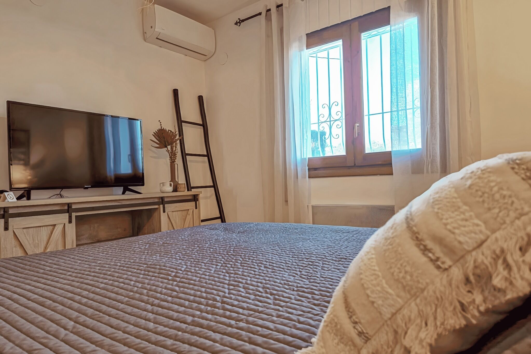 Une chambre à coucher avec un lit, un téléviseur à écran plat, une fenêtre avec des barreaux et une échelle.