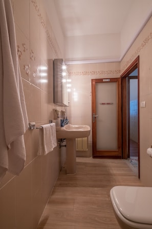 A bathroom with a toilet, sink, and mirror. There are towels hanging on a rack and a door leading to another room.