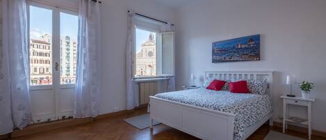 A bedroom with a bed, a window, a painting, and a nightstand.