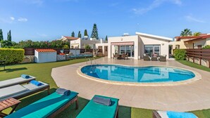 Et moderne poolområde med en rund pool, liggestole og et overdækket siddeområde.