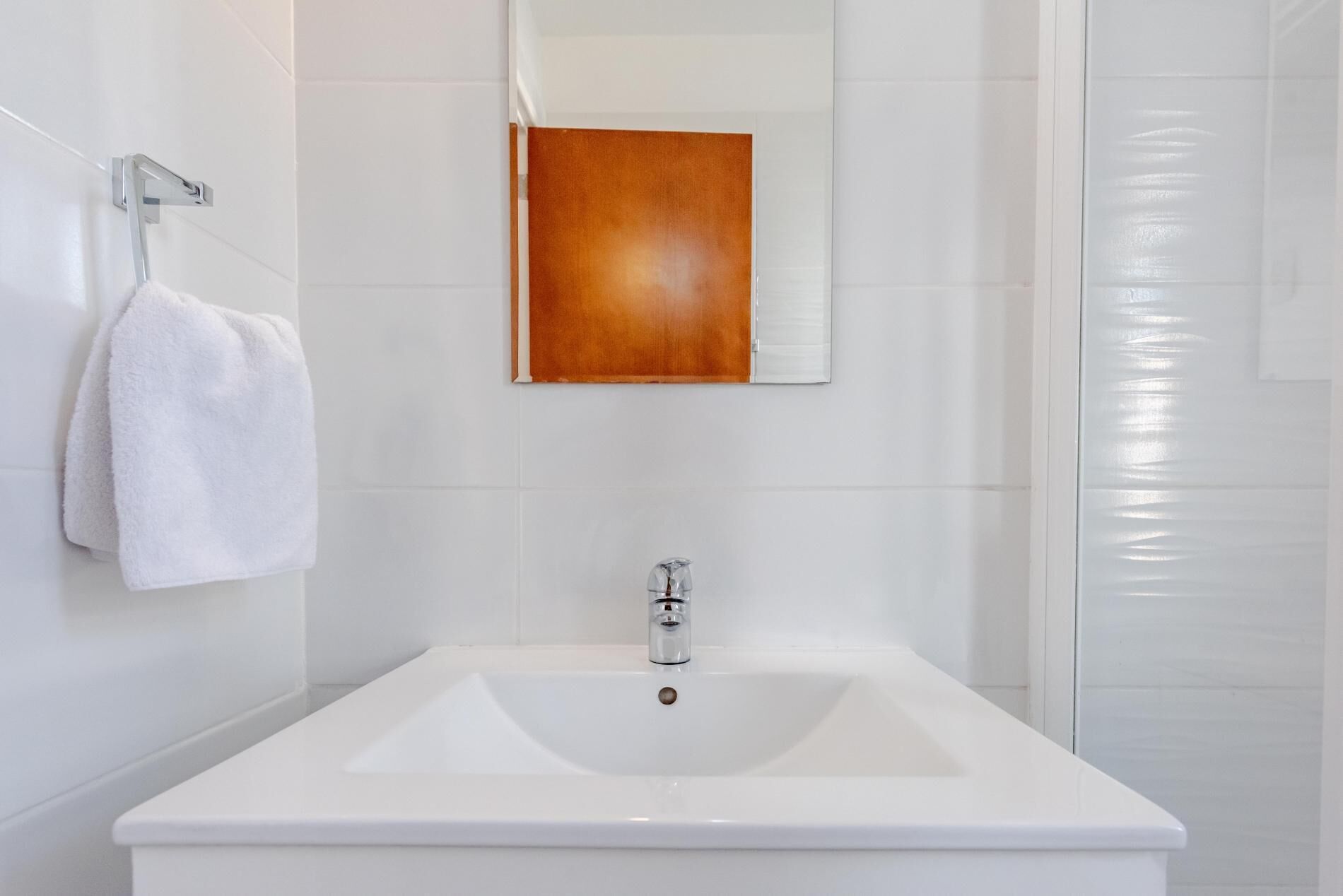 Ein Badezimmer mit einem weißen Waschbecken, einem Spiegel und einem auf einem Haken hängenden Handtuch.