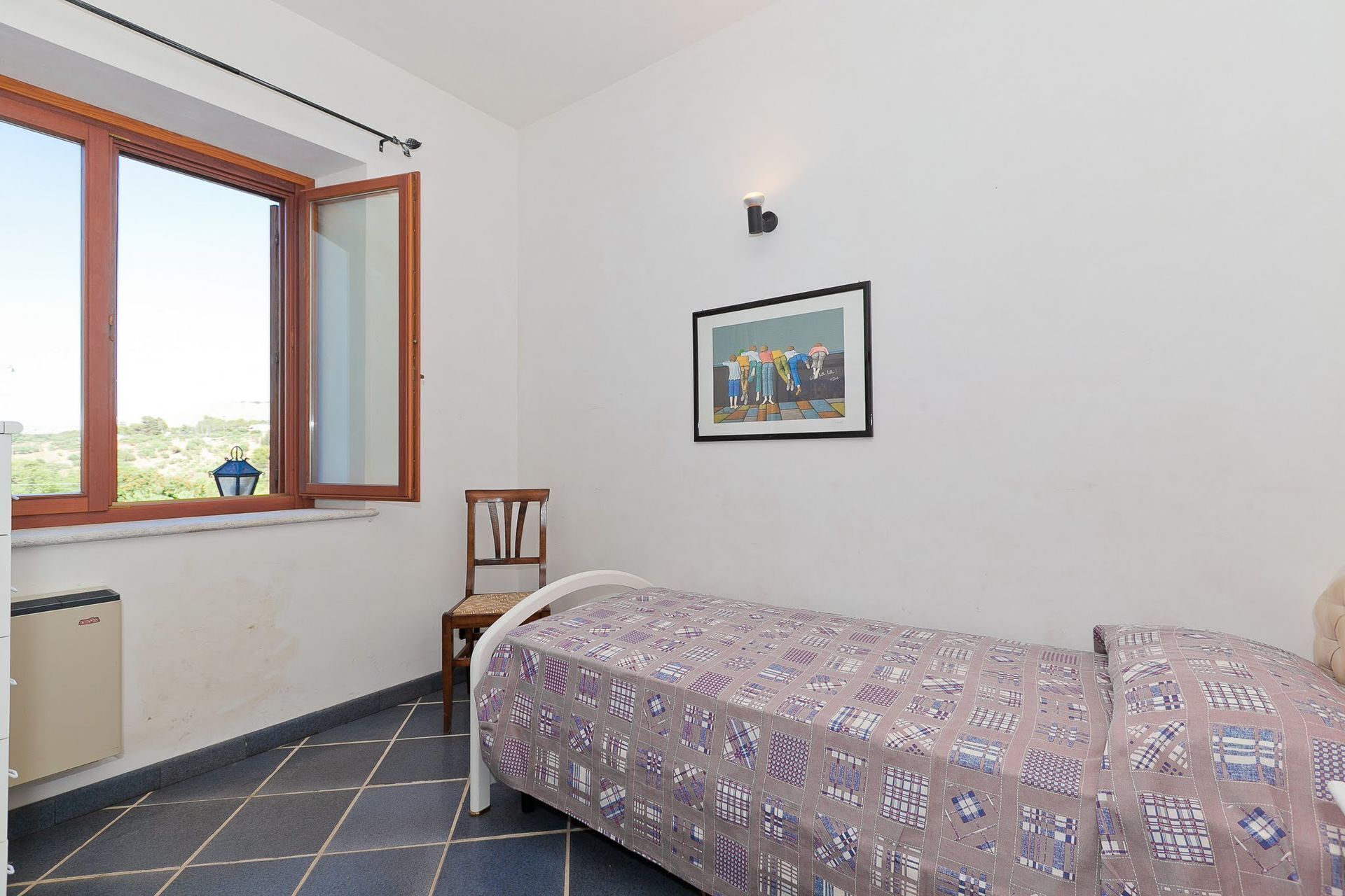 Ein kleines Zimmer mit einem Bett, einem Stuhl, einem Fenster und einem Bild an der Wand.