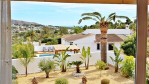 A view from a balcony overlooking a white building with a tiled roof, surrounded by various tropical plants and a small pool area. - Golondrina - panoramic hillside holiday house in Moraira (Moraira)