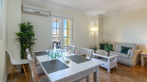 A modern living room with a dining area, featuring a sofa, chairs, a coffee table, and a dining table with glassware and a plant. - Canela Park Penthouse - Isla Canela Beach ICHP249P183 (Isla Canela)