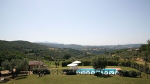 Ein Pool mit eingezäuntem Bereich, ein kleines Gebäude und Blick auf sanfte Hügel.