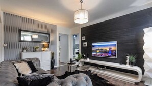 A modern living room with a large flat-screen TV mounted on a black wall, a grey sofa, a small round coffee table, and a black rug. - Luxury Villa Antoneta with Swimming Pool (Šibenik)