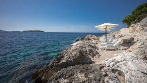 Una playa rocosa con sillones blancos y sombrillas, con vista al mar y una isla distante.