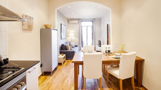 Une cuisine moderne équipée d’une cuisinière, d’une table à manger avec des chaises, et un coin salon avec un canapé et un téléviseur.