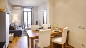 Un salon moderne avec un canapé, une table à manger et des chaises, ainsi qu’un téléviseur.