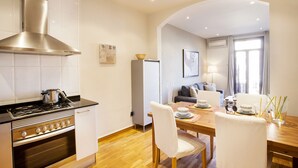 Une cuisine moderne équipée d’une cuisinière, d’un four et d’une hotte en acier inoxydable. On y trouve également un coin repas avec une table en bois et des chaises blanches.