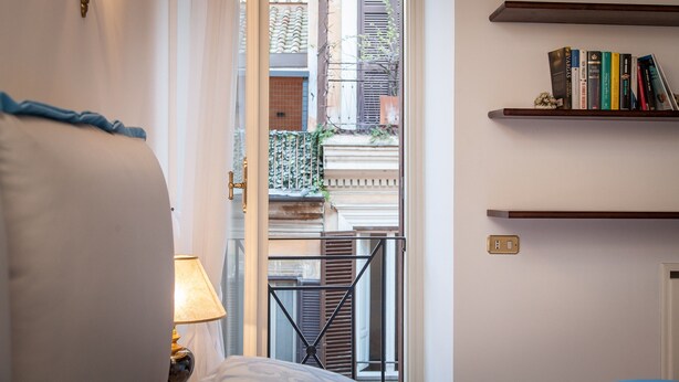 Un dormitorio con cama, mesita de noche, lámpara y estantería con libros.