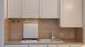 Una cocina con armarios blancos, estufa integrada, fregadero y un refrigerador pequeño.